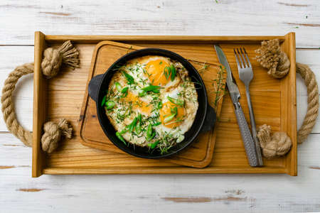 scrambled eggs with sprouts of greens and green onions in a frying pan on a wooden tray. Morning breakfast.の写真素材