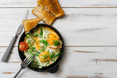 scrambled eggs with greens sprouts and green onions in a pan on a wooden background.の写真素材