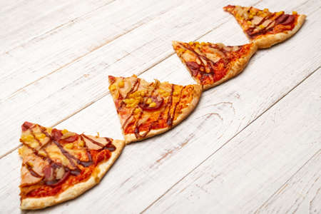 Several slices of pizza on a white wooden background.