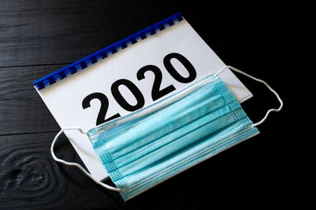 2020 numbers on paper and a medical mask on a black background. Year of quarantine concept.の写真素材