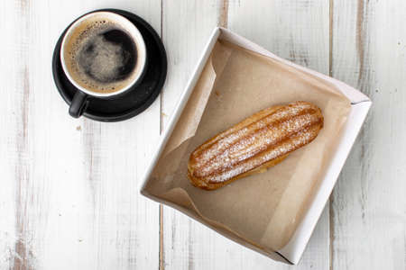 Eclair and coffee cup on a white wooden background.の写真素材