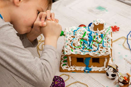 The boy makes a gingerbread house. Preparing for the holiday, creative activity.