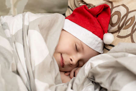 The boy sleeps in a Santa hat. Waiting for New Year, Christmas, gifts.