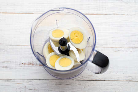 Boiled chicken eggs in a food processor, chopper on a light wooden background.