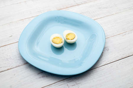 Boiled egg cut into two halves on a blue plate on a white wooden background.の写真素材