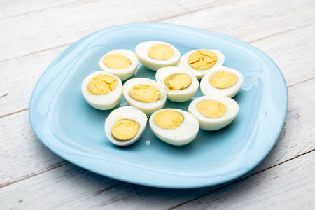 Boiled eggs cut into two halves on a blue plate on a white wooden background.の写真素材