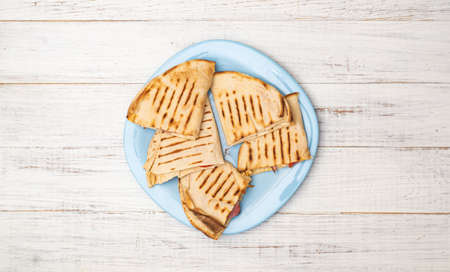 Pita, tortilla with cheese and ham on a plate on a white wooden background. A light, healthy snack.