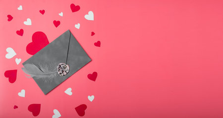 Gray envelope with a feather on a red background with hearts. Love letter concept for Valentine's...