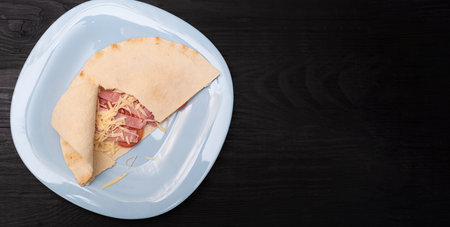 Tortilla with cheese and ham. Pita with grated cheese, ham, tomatoes on a plate.の写真素材