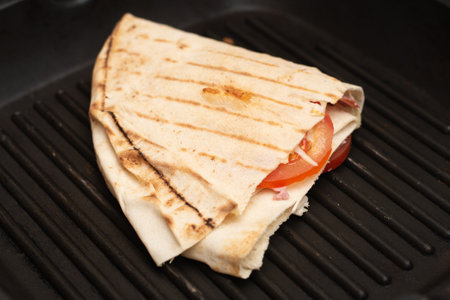 Tortilla with cheese and ham. Pita with grated cheese, ham, tomatoes on a grill pan.の写真素材