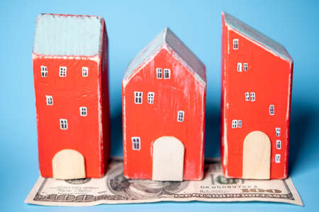 Real estate and money. Wooden toy houses and a hundred dollar bill on a blue background. Savings for home construction, mortgage, rental housing concept.の写真素材