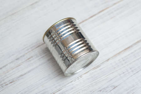 Closed metal can of canned food on a white wooden background.