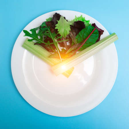 Intermittent fasting, diet concept. Figurative image of meal time. Fresh vegetables on a white plate as a clock face on a light blue background.の写真素材