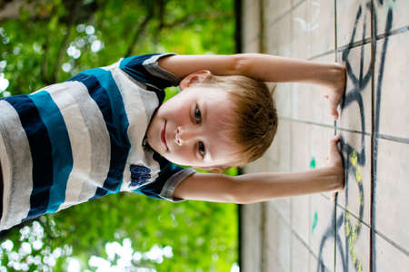 The boy climbs a tree and the wall of a building on the street.