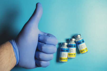 Danger, fear of vaccination coronavirus concept. A hand in a glove holds an OK sign on the background of a vaccine with a warning of danger.の写真素材
