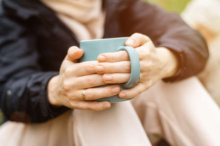 Woman with a cup in the forest, park in cool weather on a green background of foliage. Relaxation in nature, rest.の写真素材