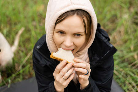 An adult attractive woman eats a sandwich outdoors in the forest, park. Snack on a hike, on a walk.の写真素材