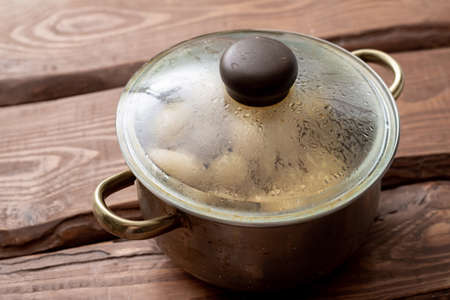 Freshly cooked young small potatoes in a saucepan with steam on a wooden background.の写真素材