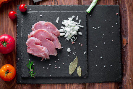 Chunks of sliced raw turkey meat, chopped onions, on a black slate background.の写真素材