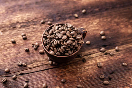 Coffee beans in a clay cup on a brown wooden old background.の写真素材