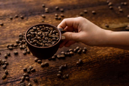 Coffee beans full cup and female hands on brown old wooden background.の写真素材