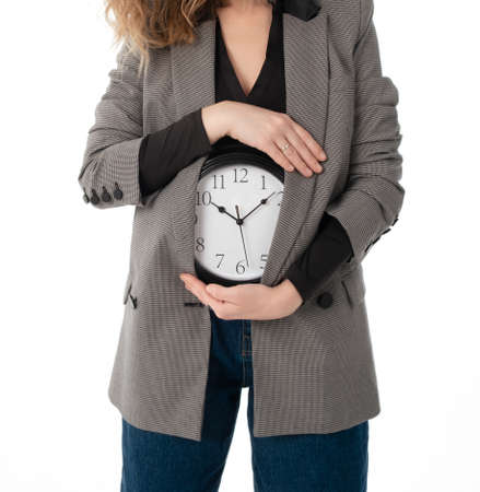 A woman holds a watch on her stomach. Pregnancy, menstruation, biological clock concept. Isolated on whiteの写真素材