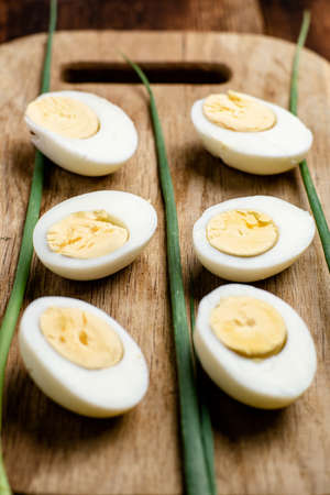 Halves of boiled chicken eggs with green onion pods on a wooden background.