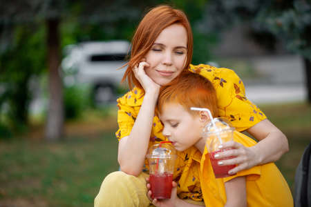 Red-haired young boy and mom are drinking red lemonade. Summer outdoor recreation.の写真素材