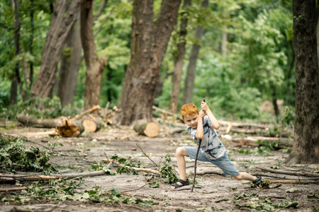 Young boy in the woods in a clearing with a wooden stick.の写真素材