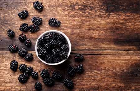 Fresh blackberries in a white bowl on a black plate on a wooden background close-up. Place for your text.の写真素材