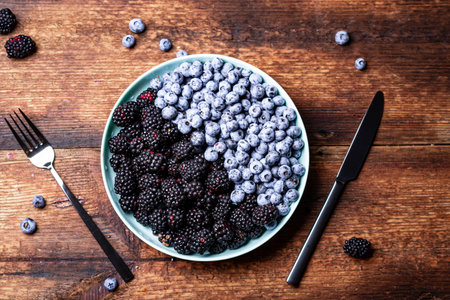 blueberries and blackberries on a plate on a dark wooden background with cutlery. The concept of vegetarianism, healthy food.の写真素材
