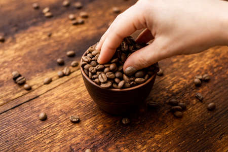 Coffee beans full cup and female hands on brown old wooden background.の写真素材