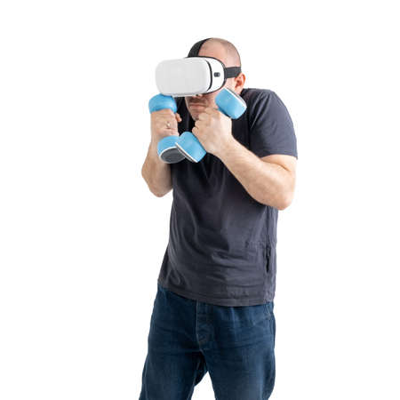 Unsportsmanlike middle-aged man wearing virtual reality glasses with dumbbells. Isolated on a white...
