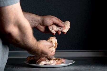 A man rubs chicken wings with spices for cooking.の写真素材