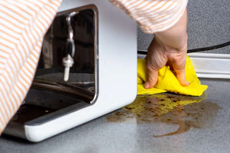 The coffee machine has broken down and needs to be repaired. The woman wipes the consequences with a...