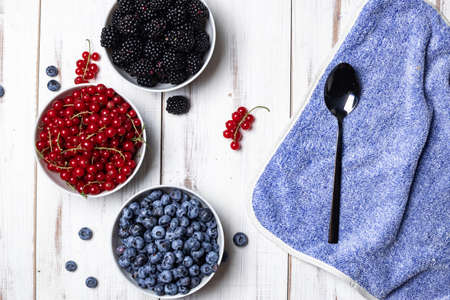 Fresh assorted berries in three plates - blueberries, blackberries and red currants on a white wooden background. Fruit, berry background.の写真素材