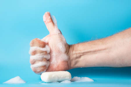 Global Handwashing Day, personal hygiene concept. A man's hand in foam holds soap on a blue background.の写真素材