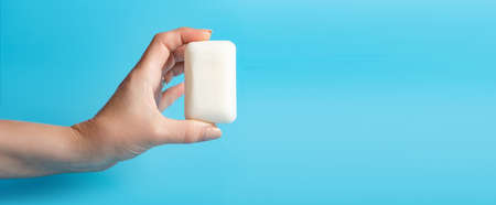 Global Handwashing Day. A bar of soap in a female hand on a blue background. Personal hygiene concept, hand washing. Banner, place for text.の写真素材