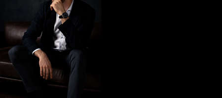 Unrecognizable stylish macho man sits relaxed on the sofa in the dark. Banner, place for text.の写真素材