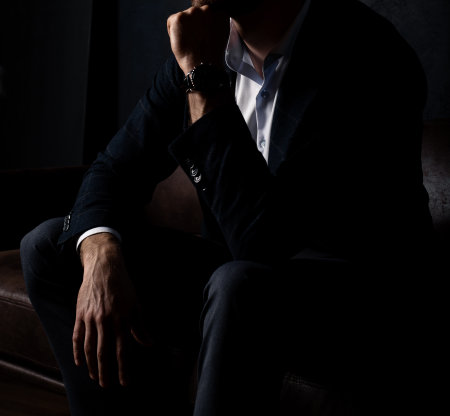 An unrecognizable man in stylish clothes sits relaxed on the sofa in the dark.の写真素材