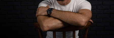 An unrecognizable man in a white T-shirt with a watch on his arm sits on a chair.の写真素材