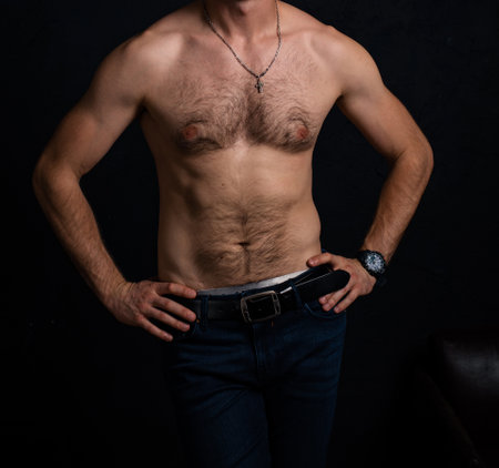A naked torso with hair of an ordinary man in good physical shape in jeans on a dark background.の写真素材
