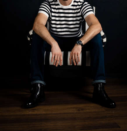 An unrecognizable man in a striped T-shirt sits on a striped armchair.