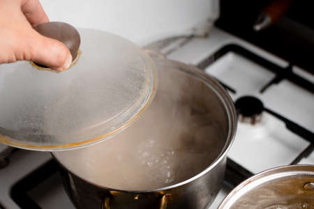 An old saucepan with boiling water and an open lid.の写真素材