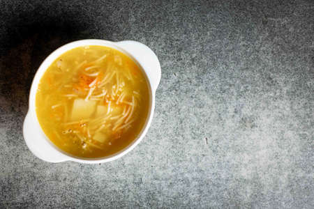 Chicken soup with noodles, potatoes, onions and carrots in a white deep plate on a gray background. Place for your text.の写真素材