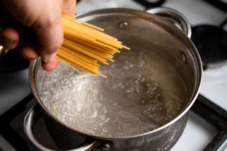 Boiling water in a saucepan and spaghetti in hand. Pasta cooking.の写真素材