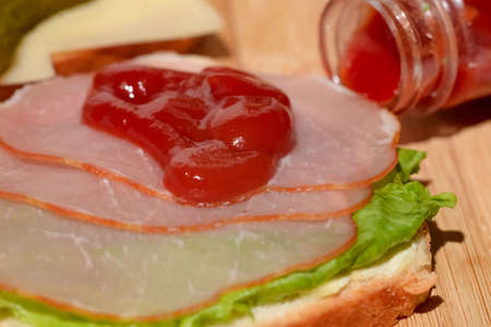 Toast with ham and a leaf of green lettuce poured with ketchup on a wooden background.の写真素材