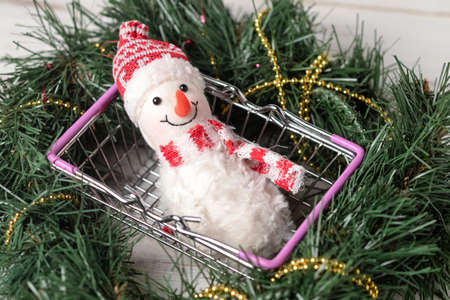 Toy snowman in a shopping basket against the background of a Christmas tree. New Years sales concept.の写真素材