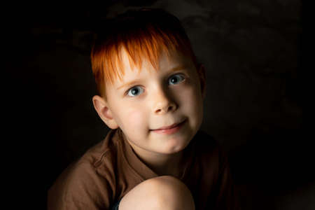 Portrait of a cute red-haired boy on a dark background.の写真素材