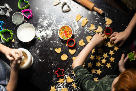 Children prepare star-shaped birthday cookies on a dark kitchen table. Family joint activity in the kitchen at home. View from above.の写真素材